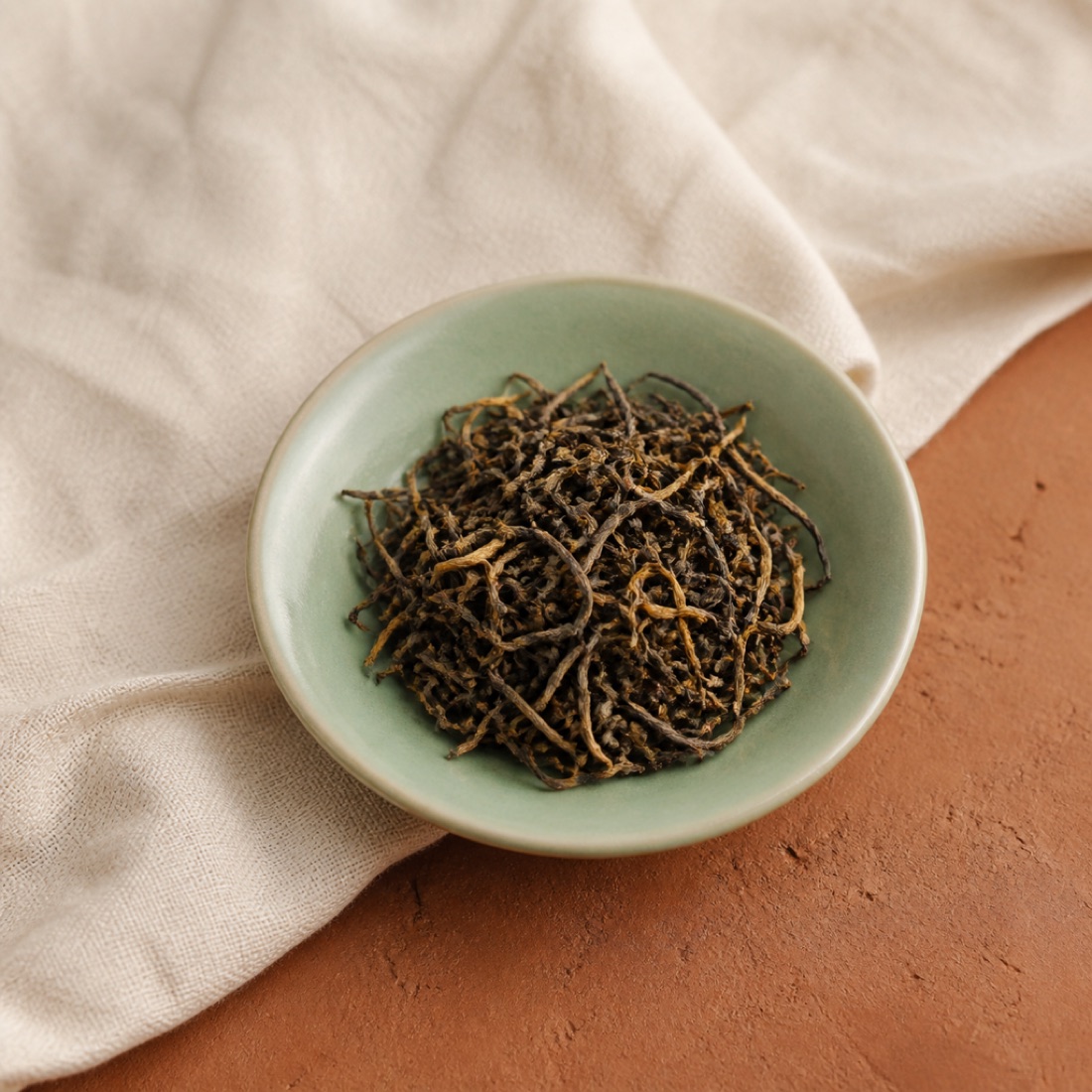 Golden-tipped dark brown black tea leaves in a celadon dish