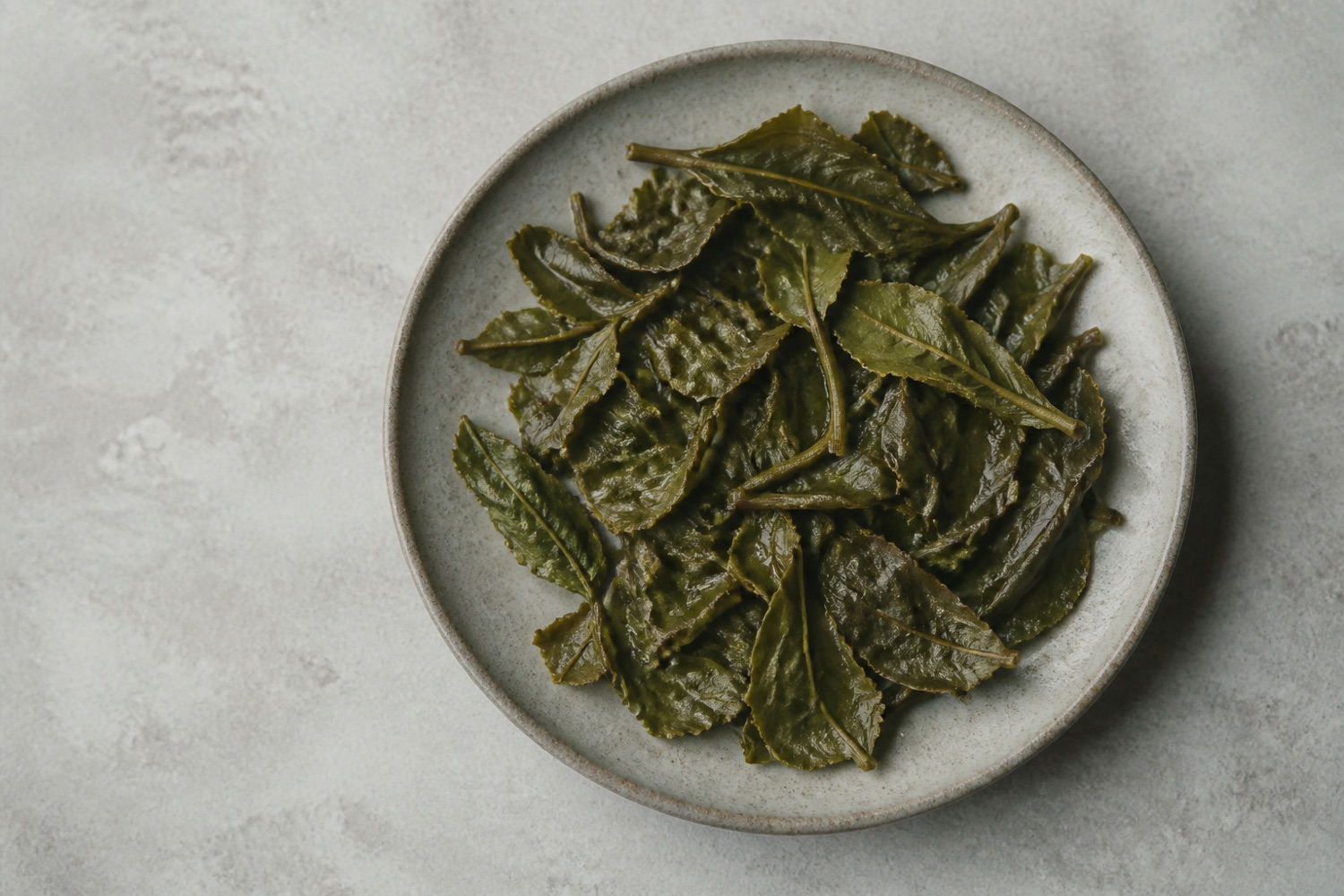 Spent wet tea leaves unfurled across a pale stone plate