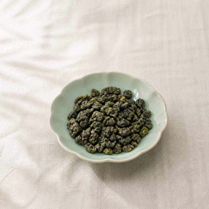 Tightly rolled emerald green high-mountain oolong pellets in a celadon dish