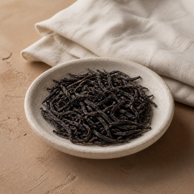 Long twisted charcoal-brown single-bush oolong leaves in a stone dish