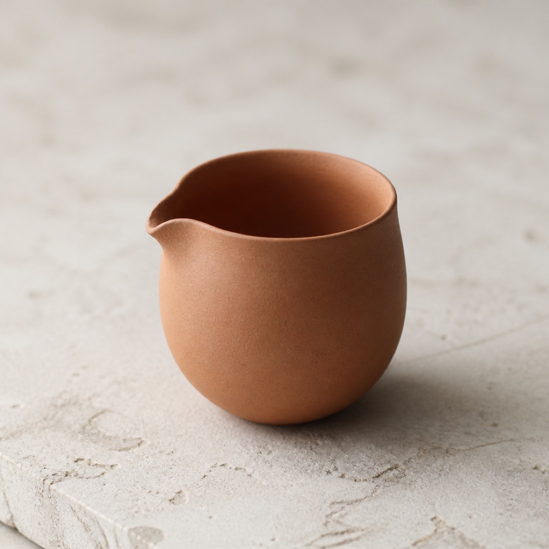 A small unglazed clay fair-cup serving pitcher on a stone slab