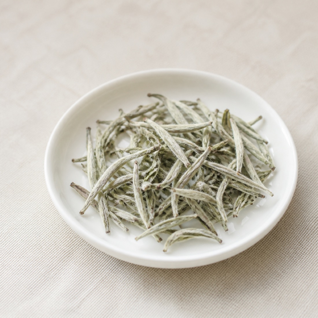 Slender silvery downy white tea buds in a white porcelain dish