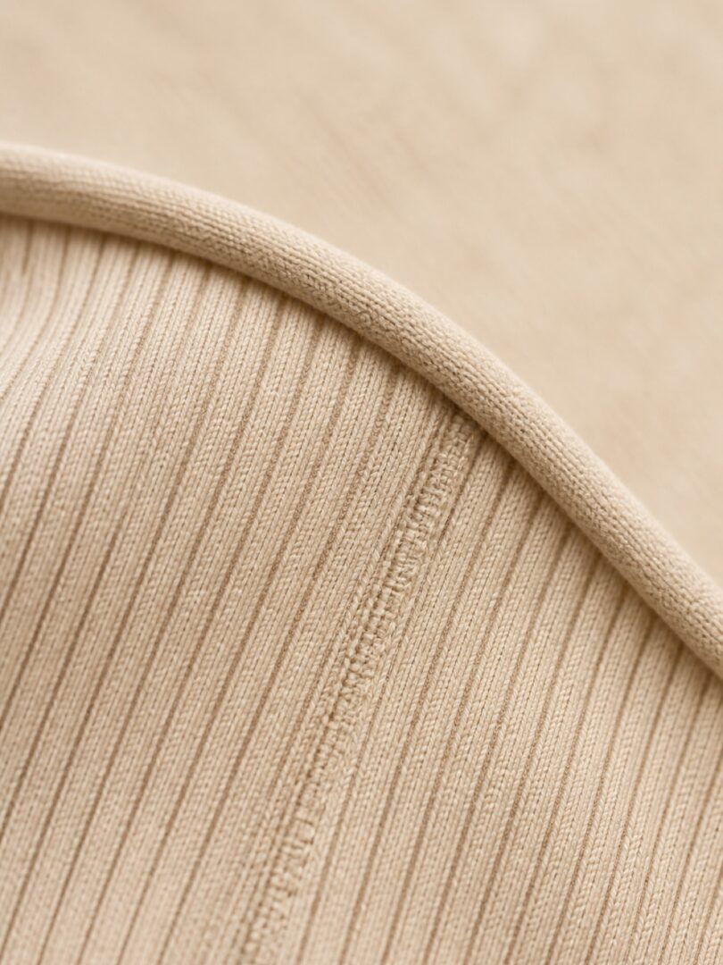 Extreme close up of oat coloured ribbed cotton knit with a flat seam