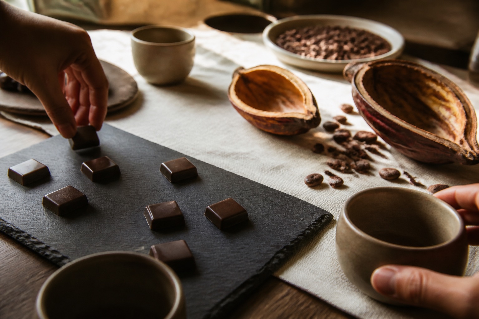 A tasting table set with chocolate squares, slate and ceramic cups.