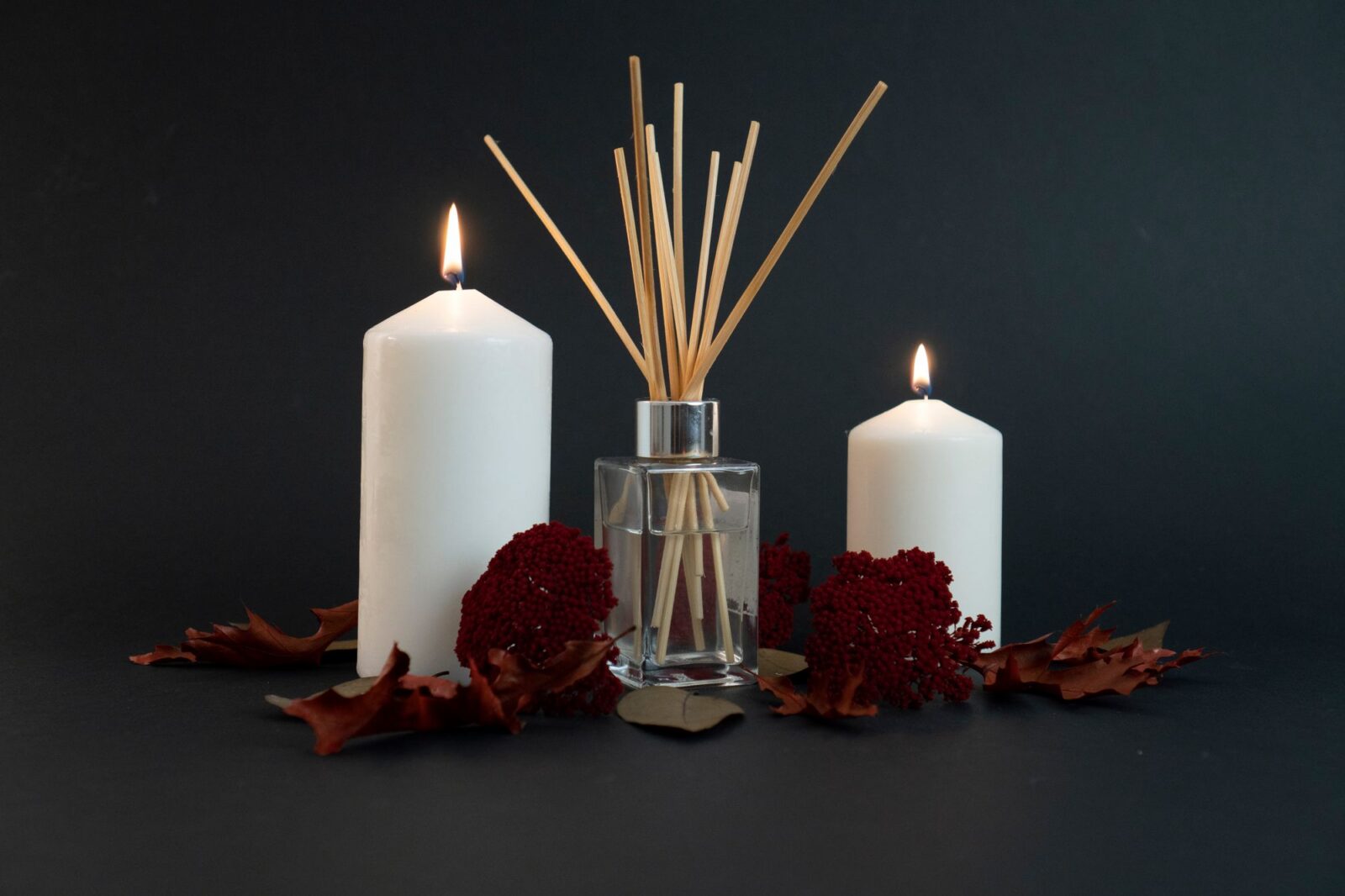Reed diffuser bottle with lit pillar candles and dried flowers